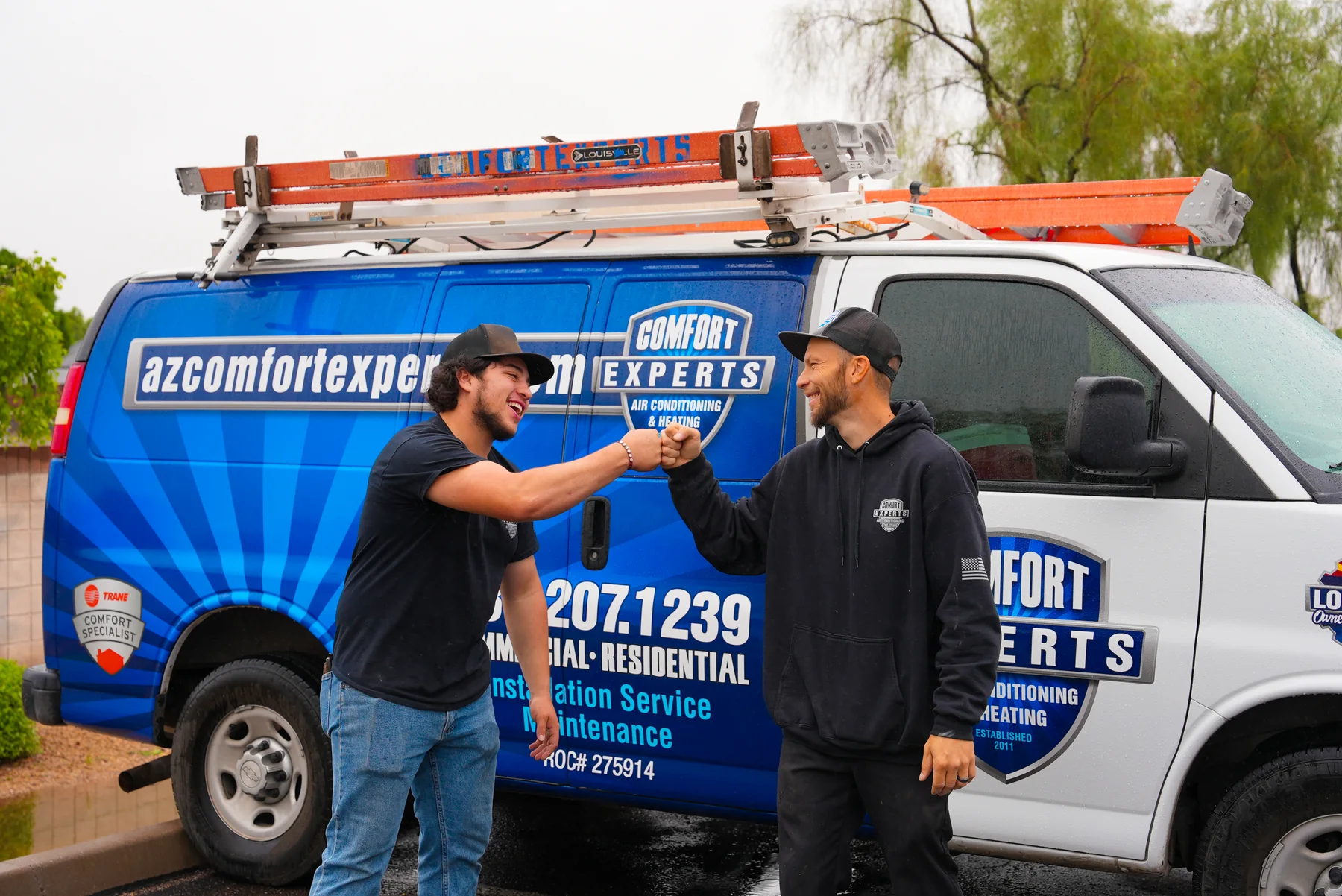Comfort Experts crew sharing a fist bump beside a branded service van
