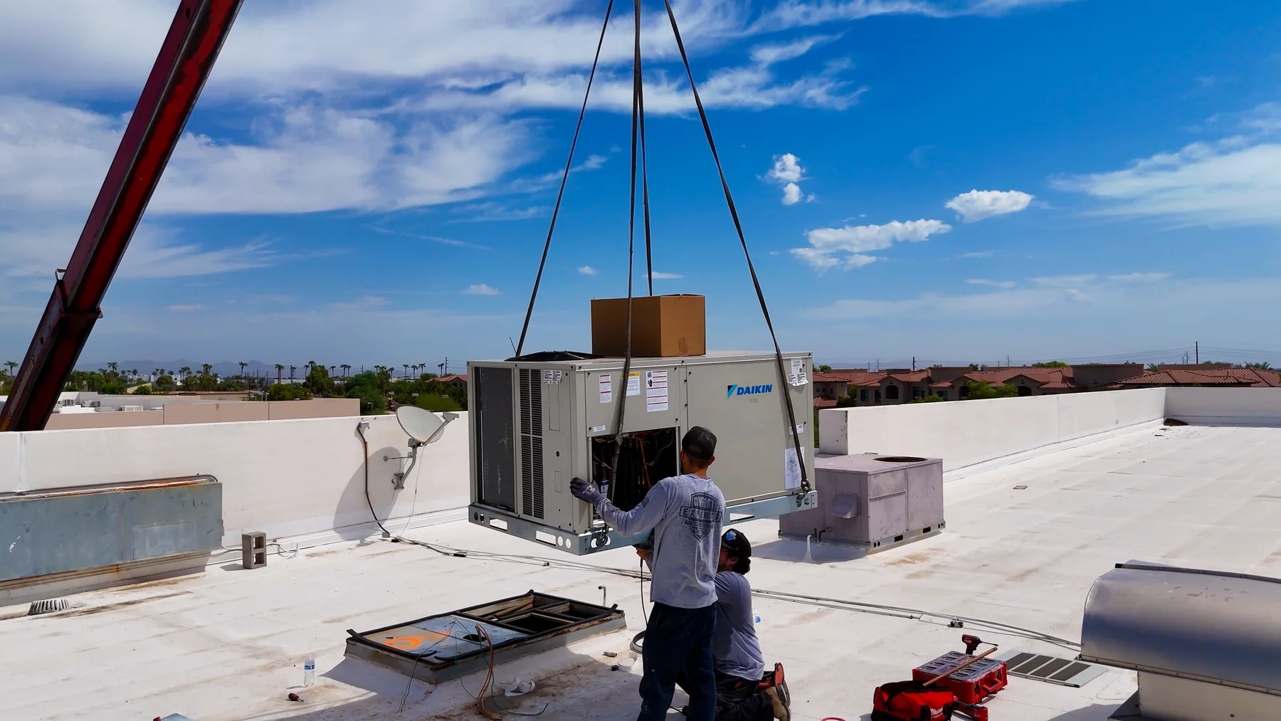 Technicians positioning a packaged rooftop unit over a roof curb