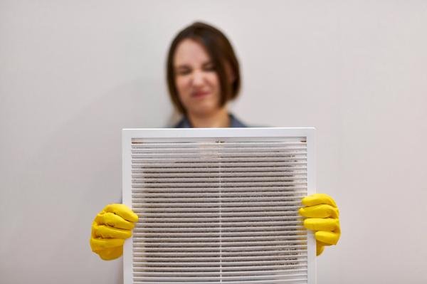 Woman holding a dirty air filter out in front of her while scrunching up her nose