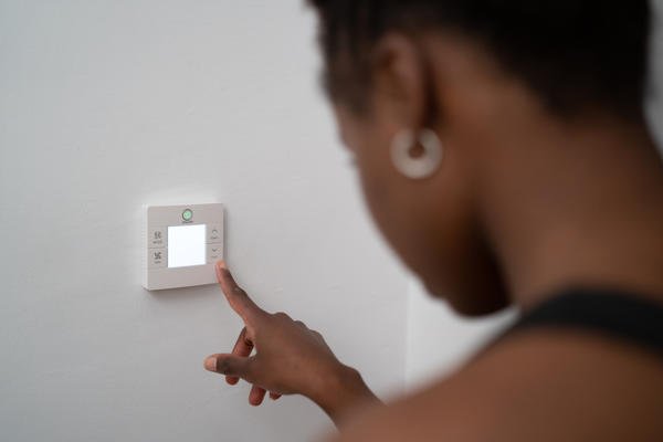 African American woman reaching to press a button on a white thermostat with a lit up LED screen.